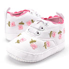 White baby shoes with pink floral embroidery on a white background