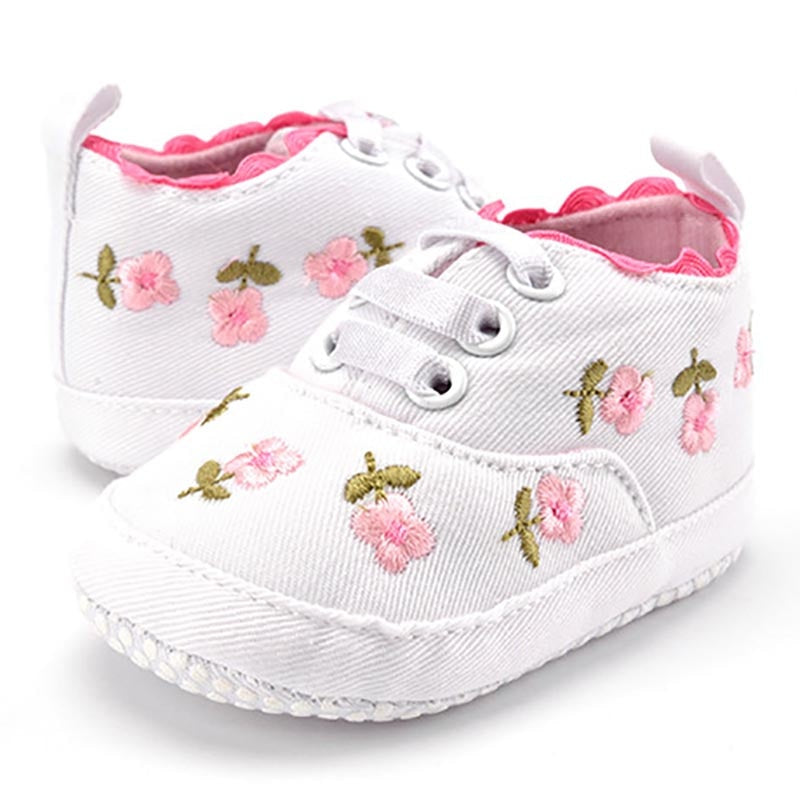 White baby shoes with pink floral embroidery on a white background