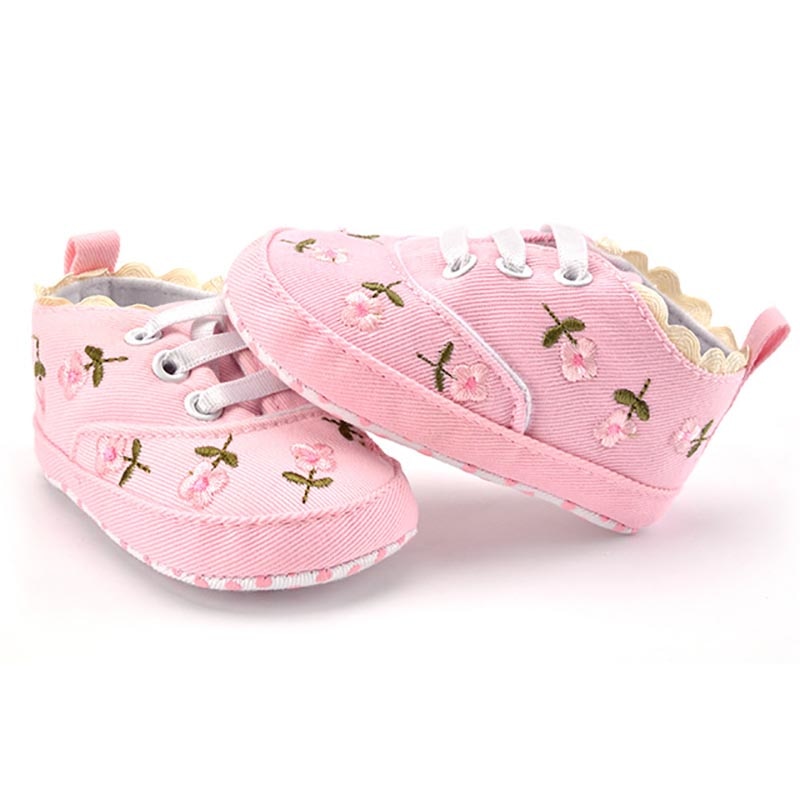 Pair of pink baby shoes with floral patterns on a white background