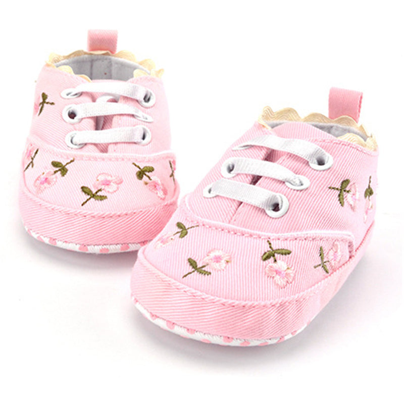 Pair of pink baby shoes with floral patterns on a white background