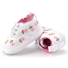 White baby shoes with pink floral embroidery on a white background