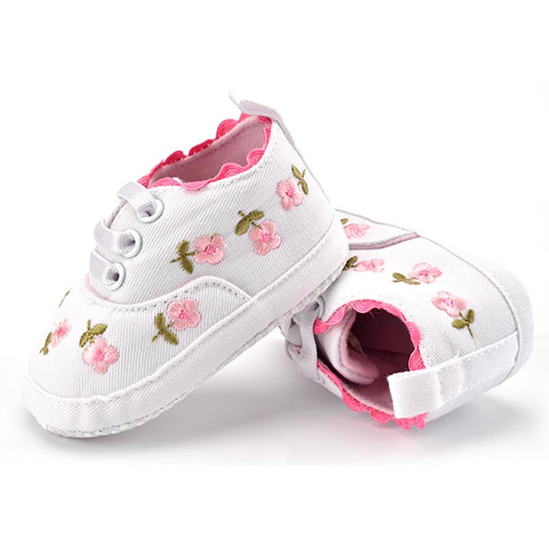 White baby shoes with pink floral embroidery on a white background