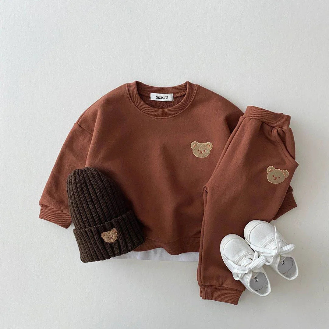 Children's brown outfit with bear embroidery, black beanie, and white sneakers on a light gray background