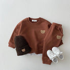 Children's brown outfit with bear embroidery, black beanie, and white sneakers on a light gray background