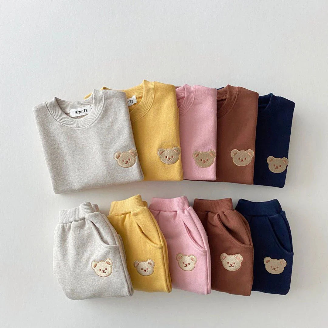 Set of folded sweaters in various colors with bear embroidery on a light gray background