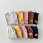 Set of folded sweaters in various colors with bear embroidery on a light gray background