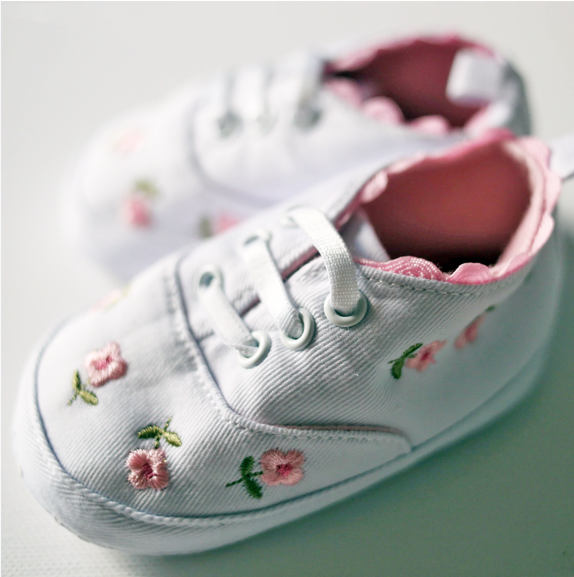 White baby shoes with floral embroidery on a light background