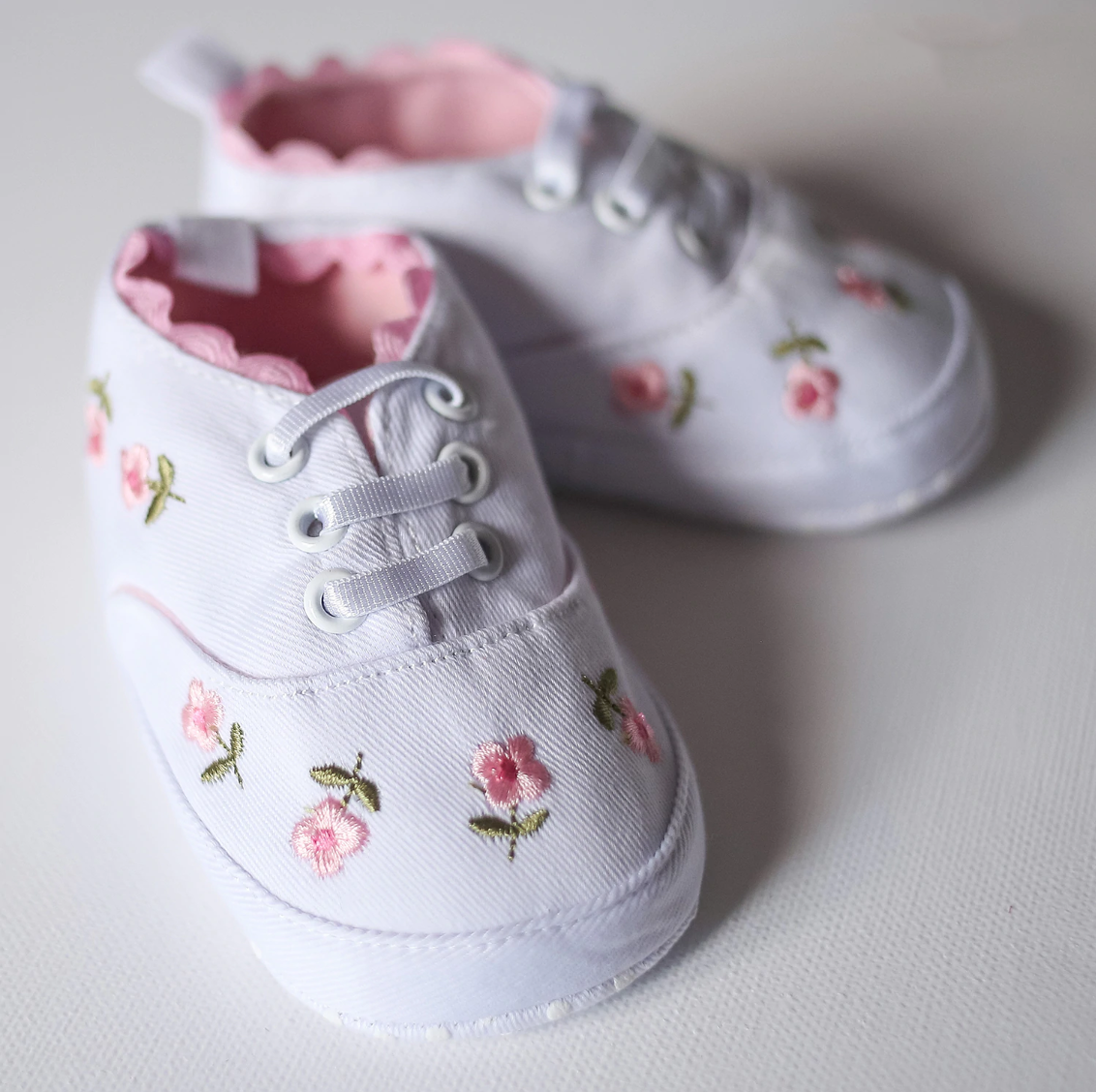 White baby shoes with floral embroidery on a light background
