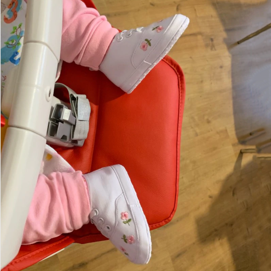 Child's feet wearing white sneakers with floral designs on a red chair.