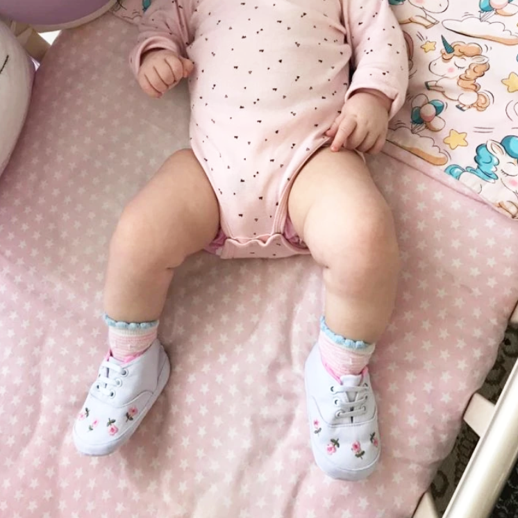 Baby in pink outfit with white shoes on a pink polka dot surface