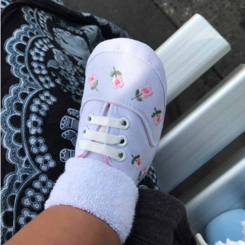 White baby shoe with floral embroidery on a bench
