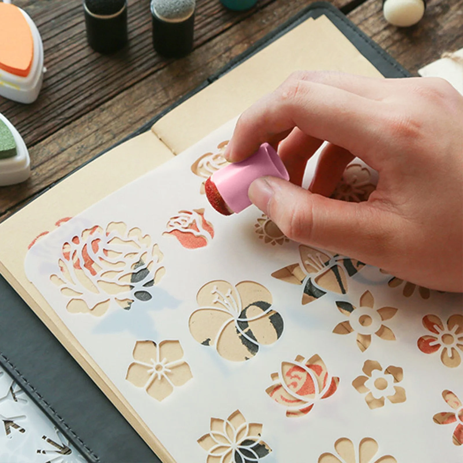 Hand using a pink stamp to create floral designs on a paper with a wooden surface in the background.