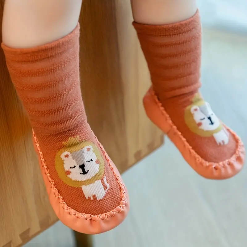 Children's orange socks with cartoon designs on a wooden floor.