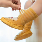 Yellow baby shoes with soft sole being worn on a white background