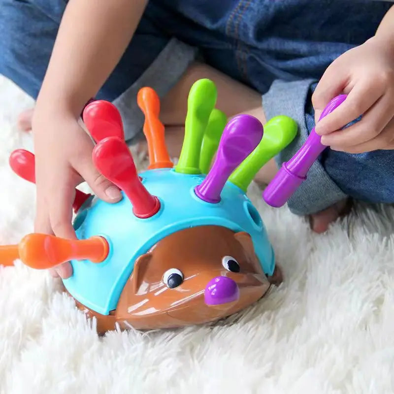 Colorful hedgehog toy with multiple sticks being played with by a child on a soft surface.