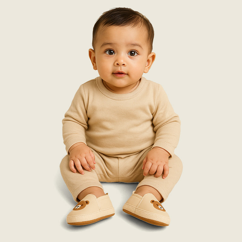 Baby wearing a beige outfit with matching shoes on a light background
