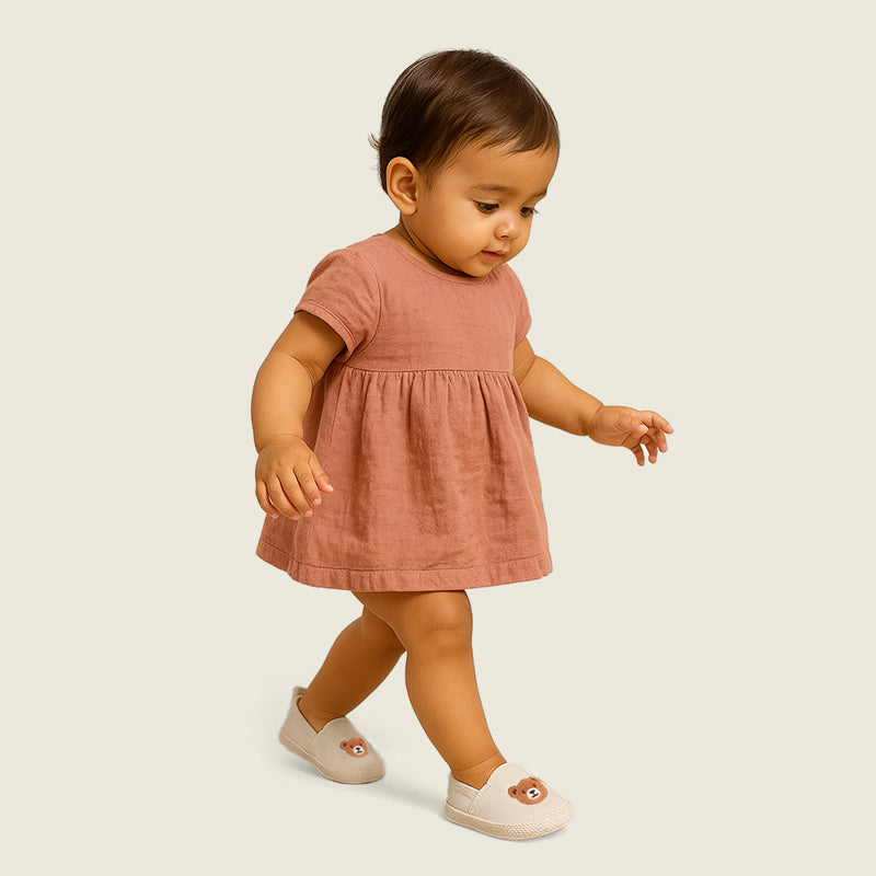 Baby in a pink dress walking on a plain background