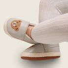 Gray slip-on shoes with a bear emblem worn by a person on a light background