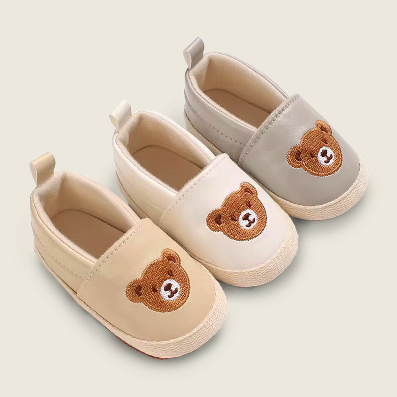 Pair of baby shoes with bear face designs on a light background