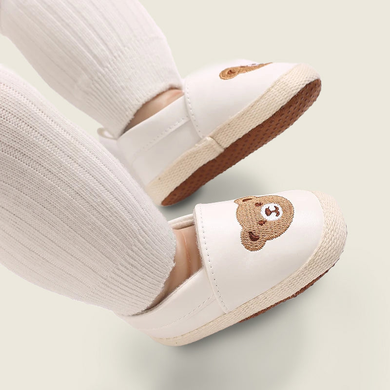 White shoes with bear embroidery worn with white socks on a light background