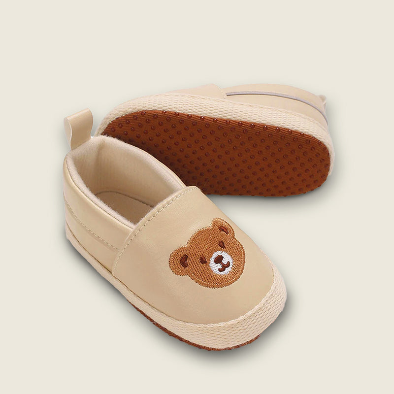Beige baby shoes with a teddy bear design on a beige background