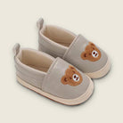 Pair of light gray baby shoes with brown bear faces on a beige background